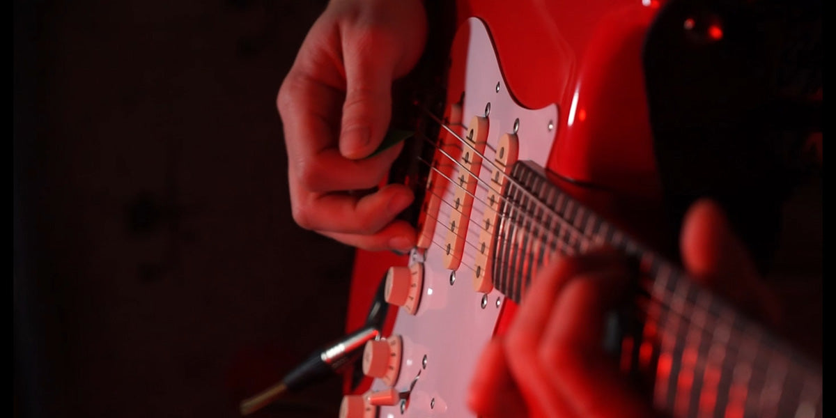 Close-up of a person playing a red electric guitar with a dark background