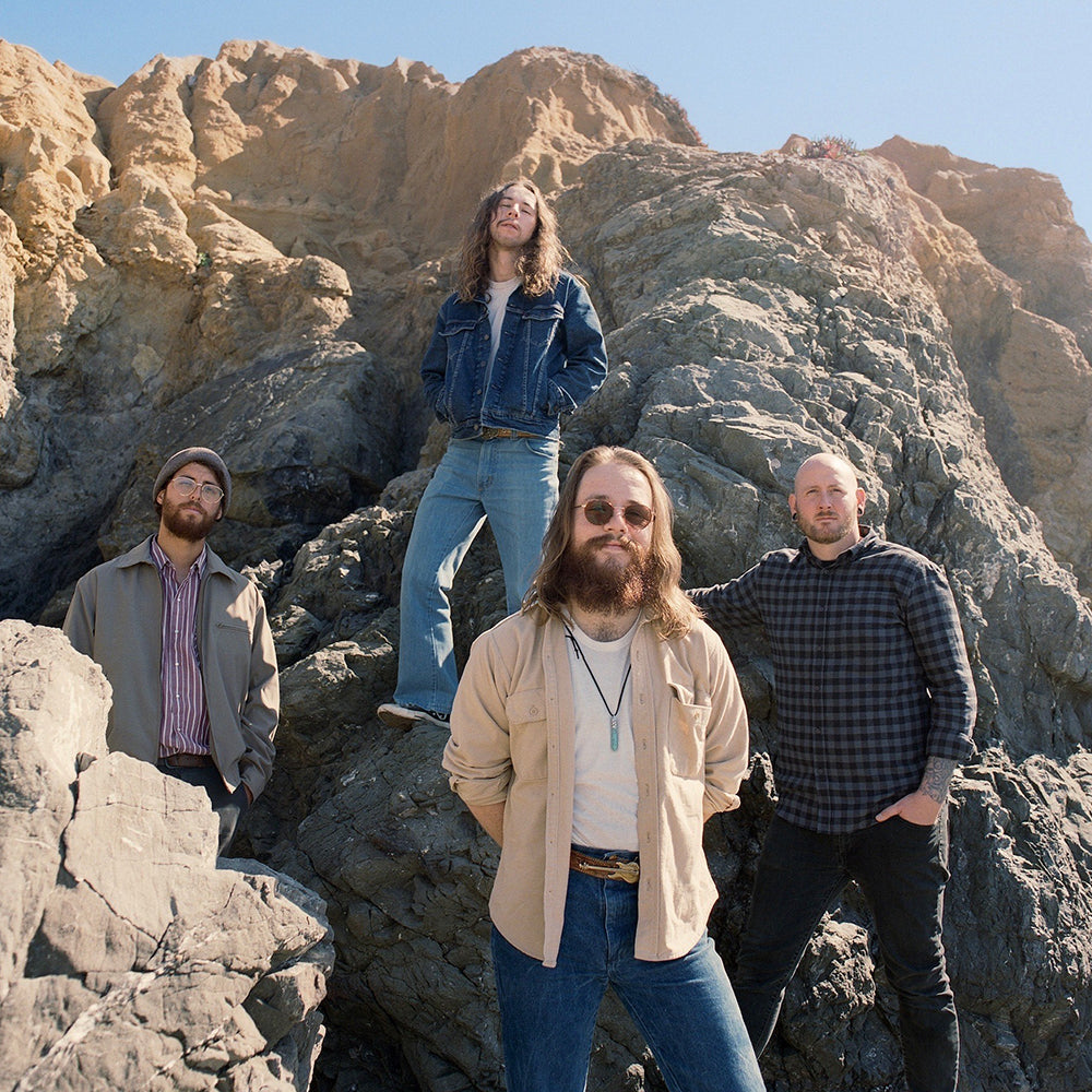 Four individuals standing on rocky terrain with a mountainous background