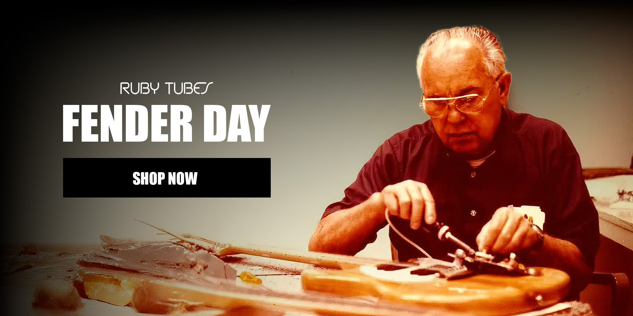 A promotional banner for 'Ruby Tubes Fender Day' featuring a man wearing safety glasses and a dark shirt working on a guitar in a workshop, with 'SHOP NOW' text on the left.